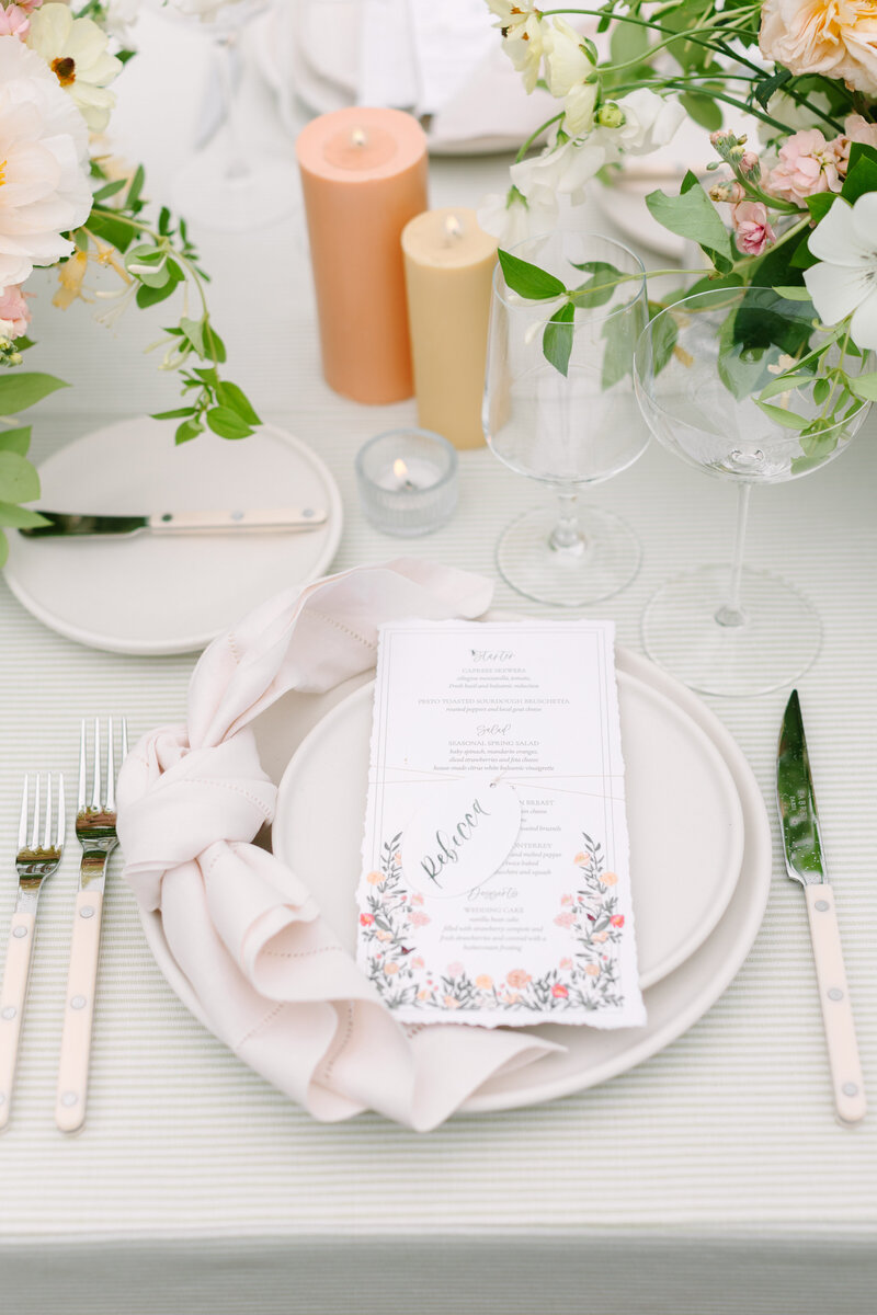 white wedding tablescape with dinner menu, peach candles, and flowers and greenery.