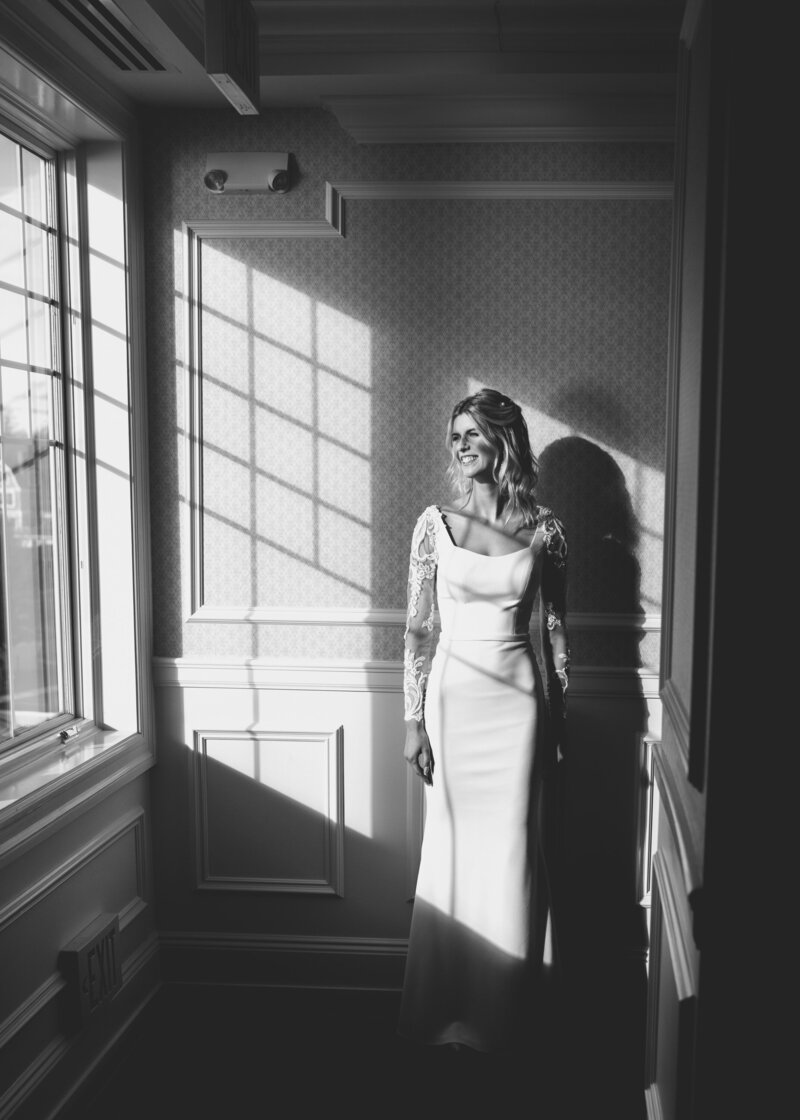 A bride smiles while looking out a window.