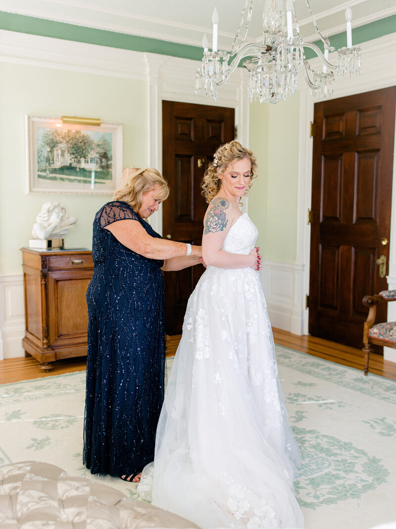 Mother of the bride in a sparkly blue dress zipping up bride's gown