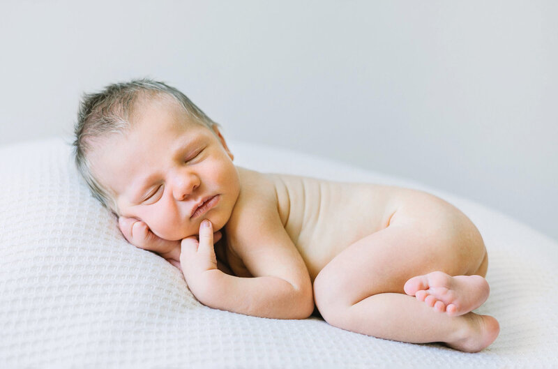 A blonde newborn baby boy posed during a newborn photography session