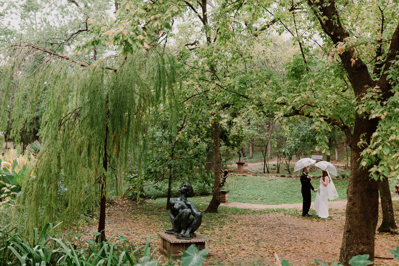 Bride and groom in woodland area holding clear umbrellas