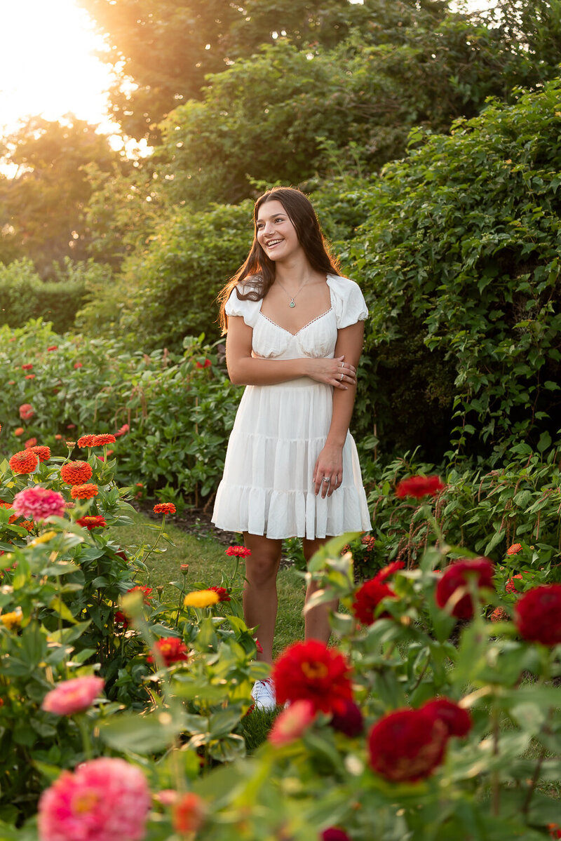 High school girl in white dress, smiling off camera in field of flowers