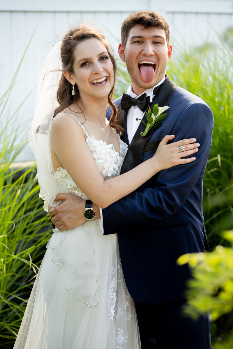 A bride and groom hugging while the groom sticks his tongue out.
