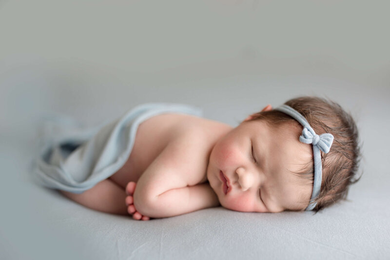Newborn girl with tiny bow on blue fabric