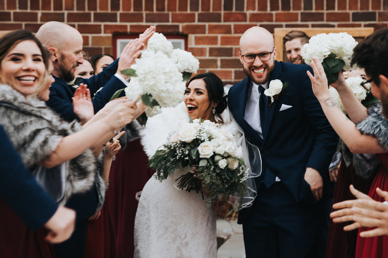 A wedding party surround an excited bride and groom and share high fives and handshakes