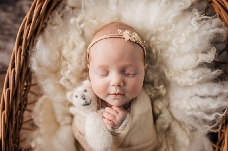 baby girl holding a teddy bear in white fluffy wool blanket in cane bed