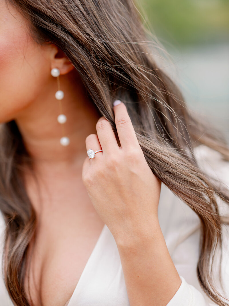 a woman wearing pearl earrings touching her dark hair with her hand showing off her  engagement ring