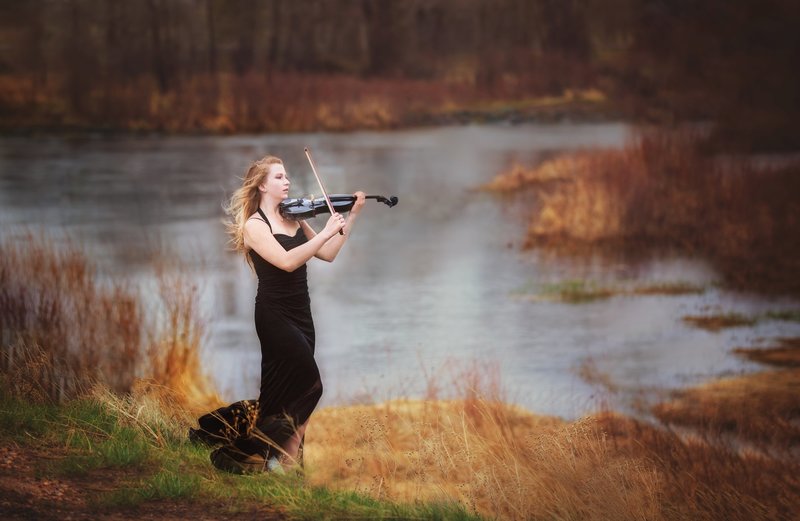 Laramie High school senior pictures of a  girl playing a black violin in the fall by the river in a black dress.