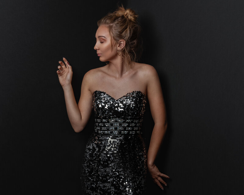 lady in black sequence dress faing sideways with hands rested on studio wall