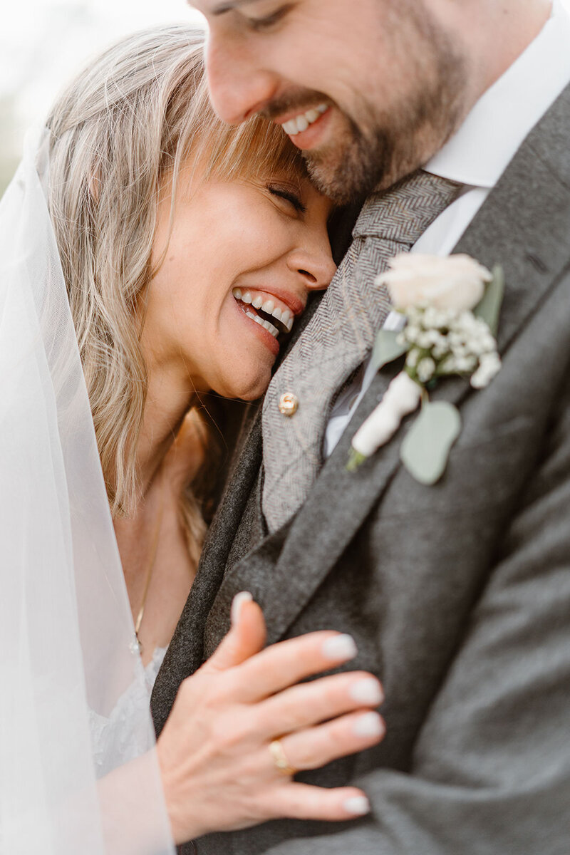 Portrait photo of the bride laughing while she's hugging the groom