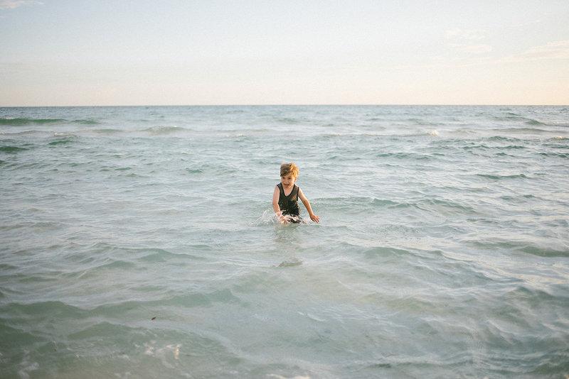 Little boy waste deep in the ocean during family vacation, captured by Laurie Baker
