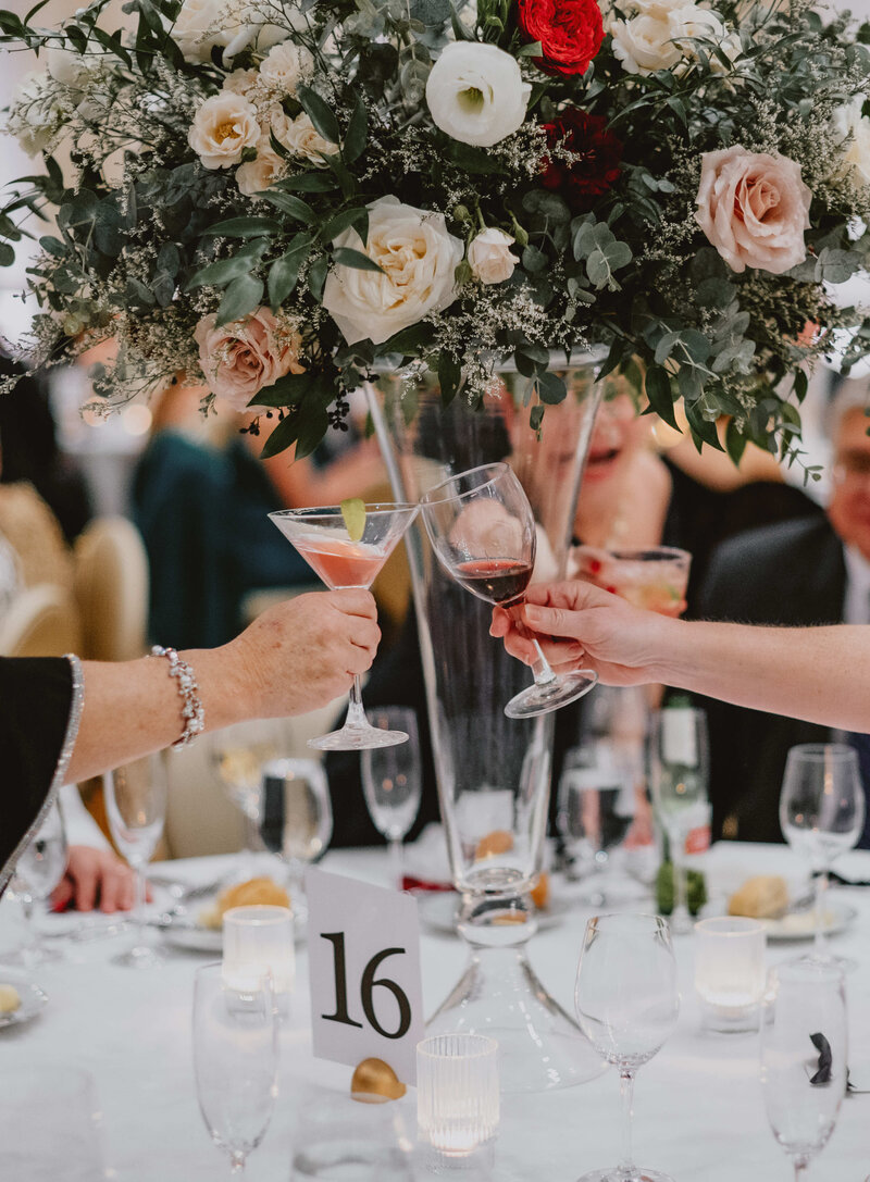 A table setting at a formal event, likely a wedding or similar celebration.  A large floral arrangement in a tall vase dominates the center of the table.