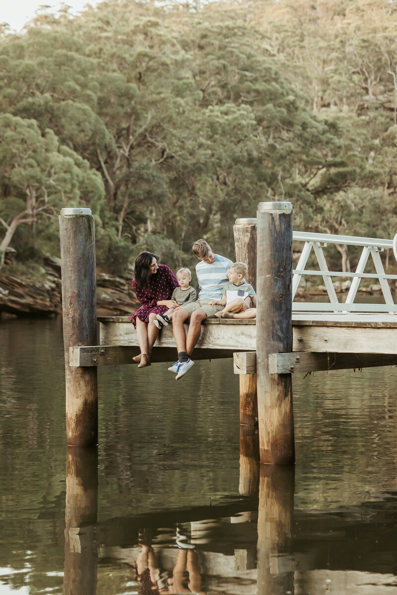 A sweet family of four sitting on a jetty on the river.