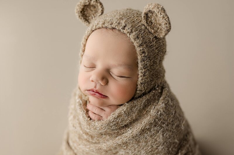 You can see all the tiny features of this newborn baby boys eyes mouth and nose as he wears a little bear bonnet