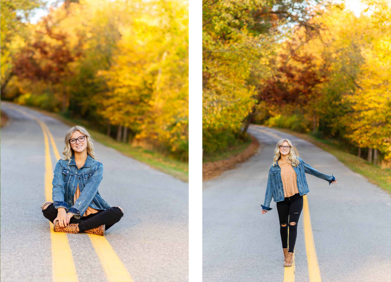 high school senior girl walking and sitting in road with fall colored trees in the background