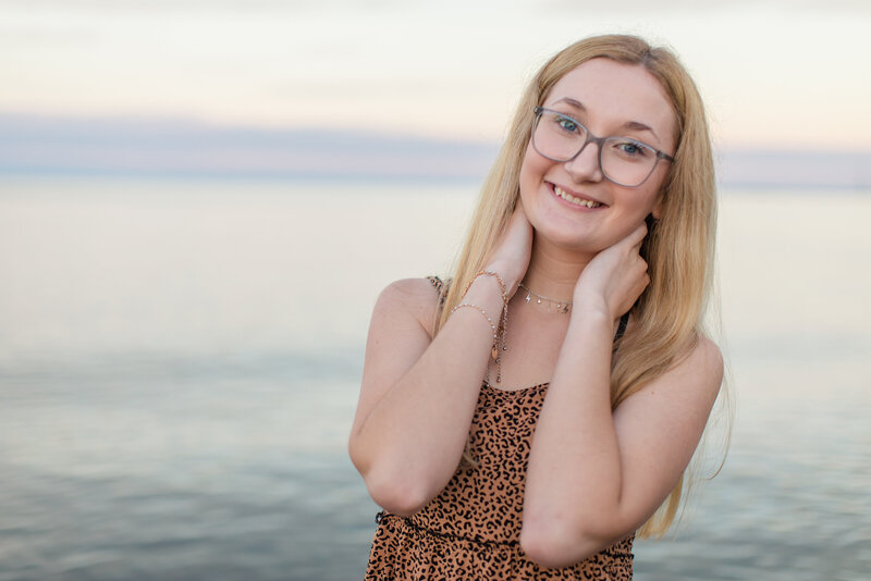 A high school senior photo of a girl smiling by the water.