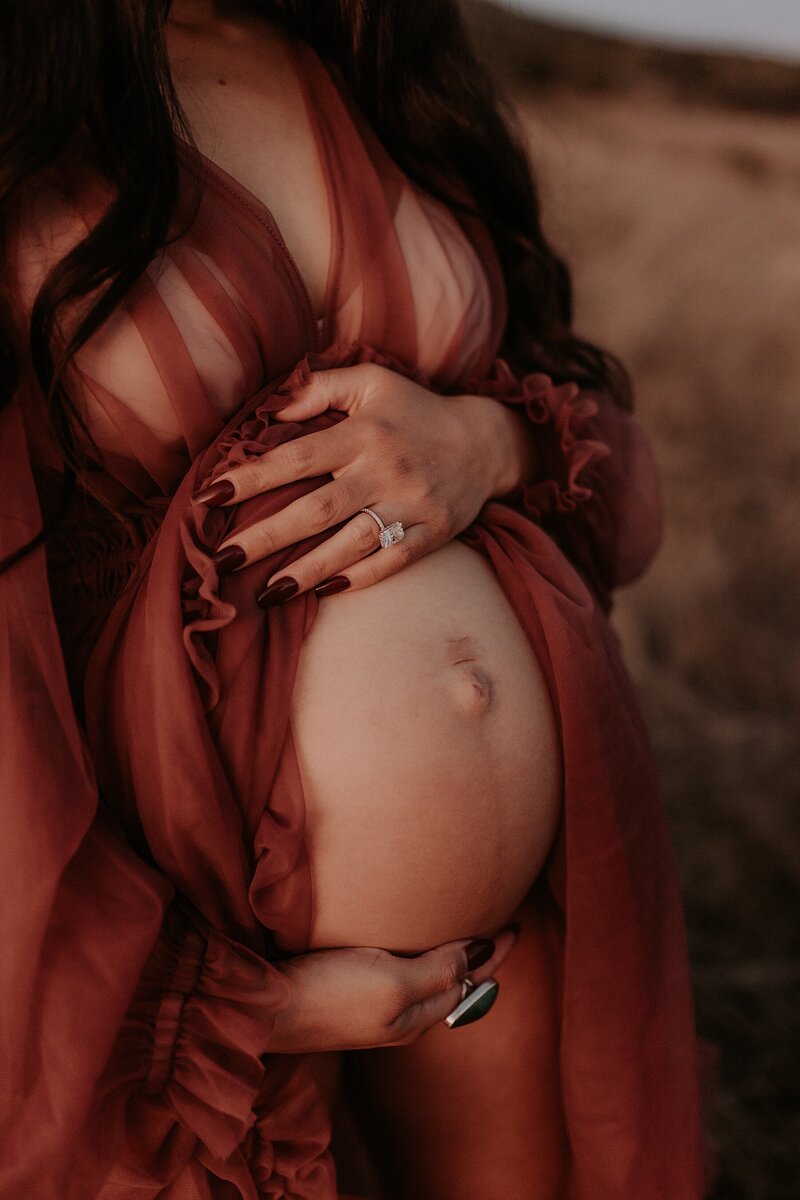 A pregnant woman in a red dress is standing in a field.