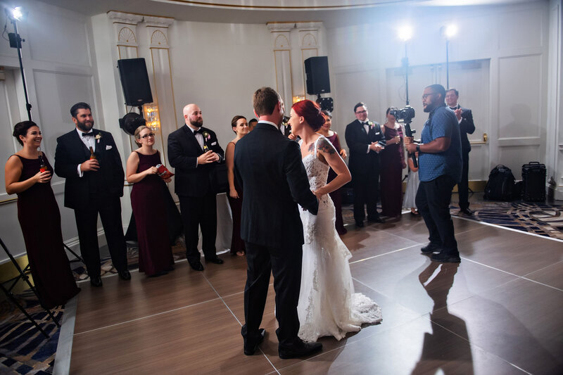 Bride and groom sharing first dance, while being videoed by wedding videographer