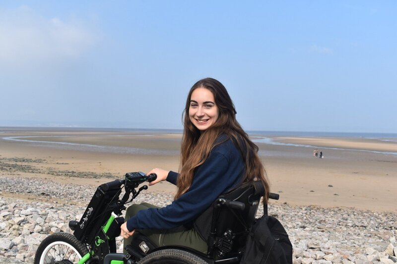 Bethany Handley on the beach in a wheelchair, smiling.