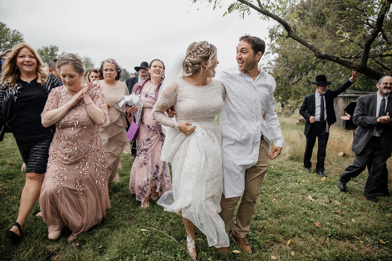 A couple dancing their way to their reception after their ceremony with family at a mansion in Maryland. The bride and groom are looking at one another smiling, and the whole group is full of ecstatic energy.