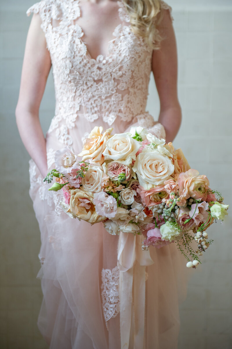 bride in blush dress holds full bouquet of flowers