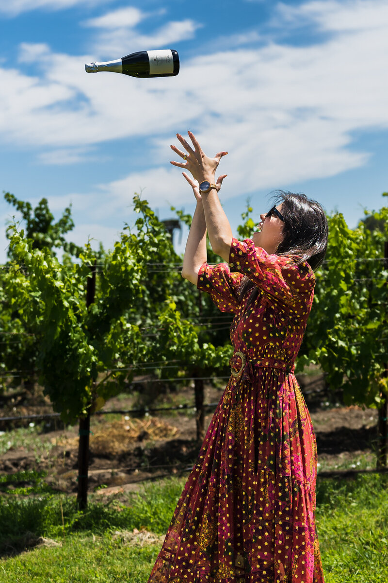 Woman plays and throws a wine bottle to the air,  in a vineyard in Napa-CA