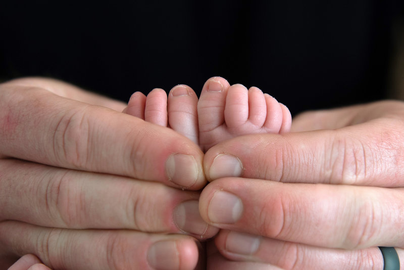 Newborn baby girls feet held by Dad's large fingers.