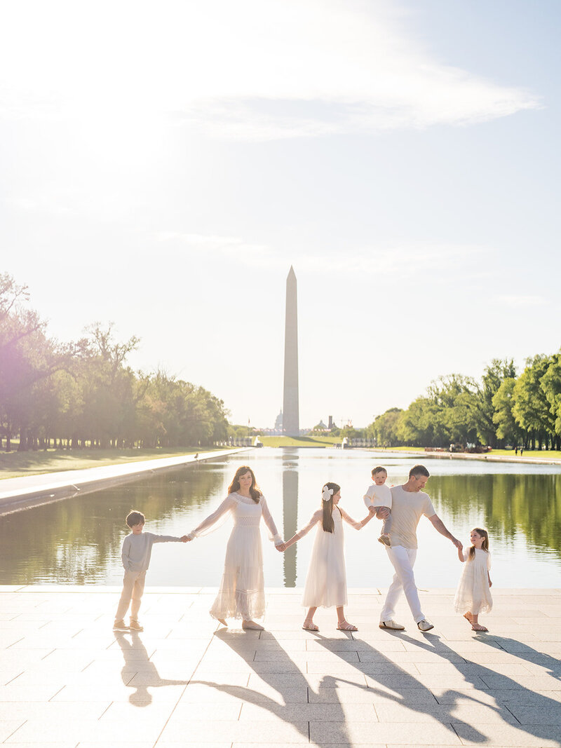 Family of six hold hands and walk across reflecting pool by the Lincoln Memorial in Washington DC.