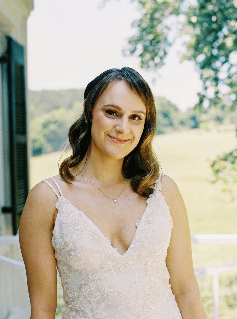 A bride in a white lace dress in Virginia has natural makeup standing outside