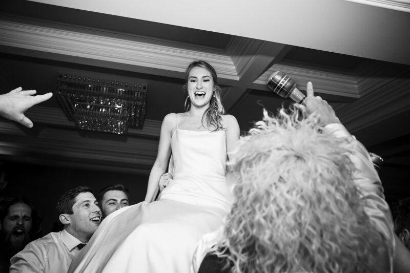 Black and white photo of a bride being carried by her guests at her ballroom wedding reception at La Valencia Hotel in San Diego.