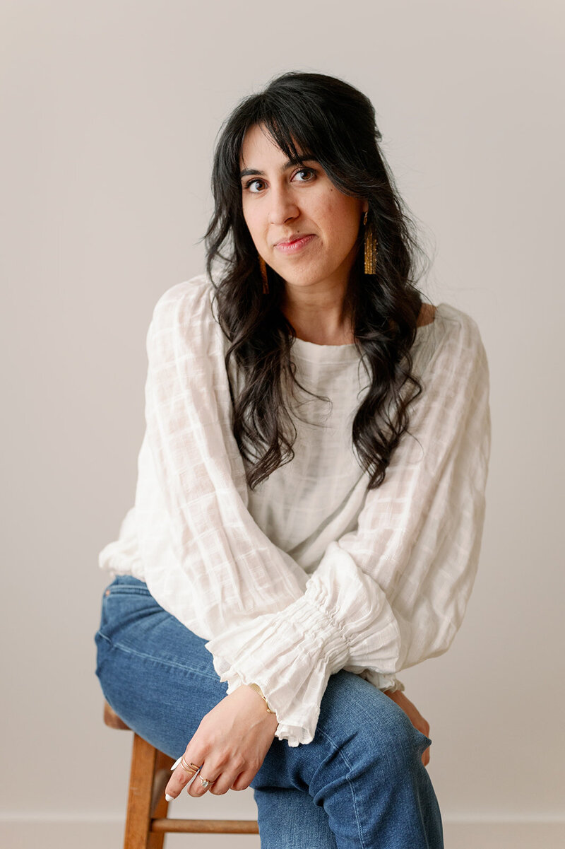 Woman sitting on a stool wearing a white top and blue jeans