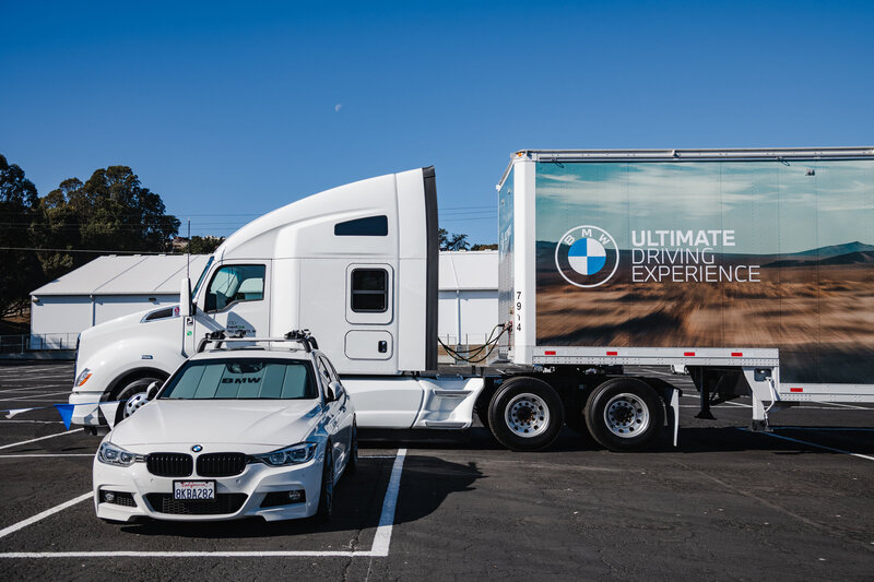 A semi with the words BMW Ultimate Driving Experience sits parked behind a white BMW in San Francisco, CA