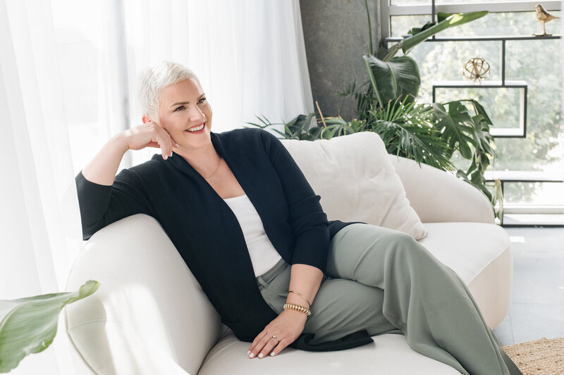 Amy Dewaele sitting on a couch in a living room and smiling at something off to the side.