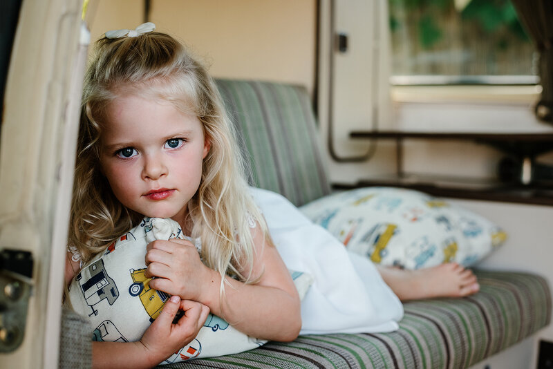 Young girl in white dress lays on backseat of retro camper van.