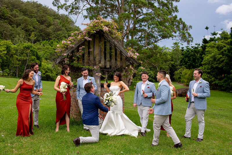 Funny groom kneeling in front of the bride with a bouquet of flowers