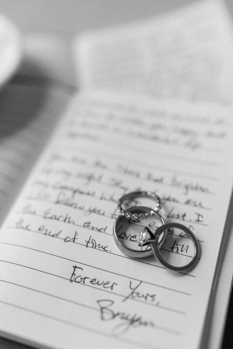 Wedding rings laid on a small book that contains handwritten wedding vows.