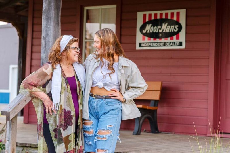 Two women chatting happily near a wooden building with a "hoorman's independent dealer" sign.