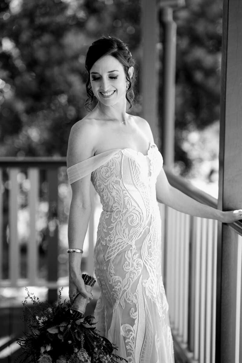 Beautiful bride poses at the balcony with her wedding dress and a bouquet
