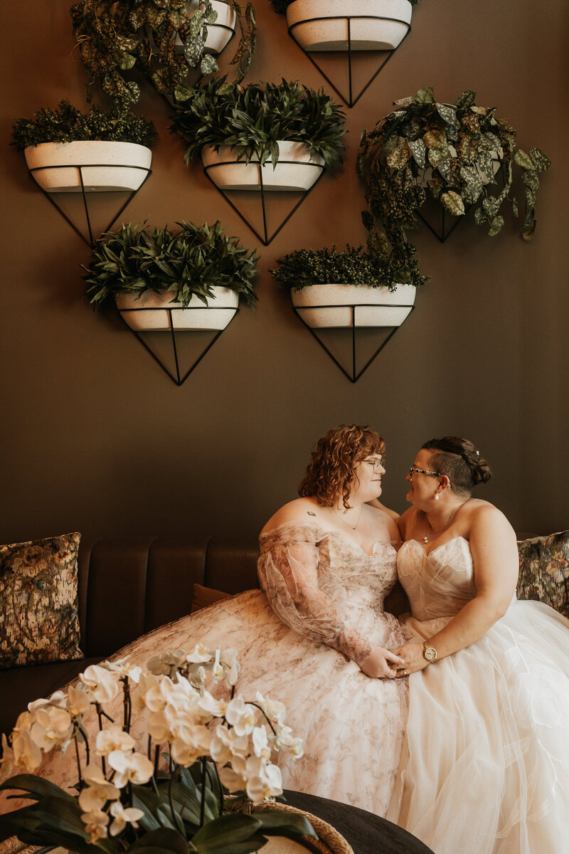 A newlywed couple sitting on a couch together holding hands 