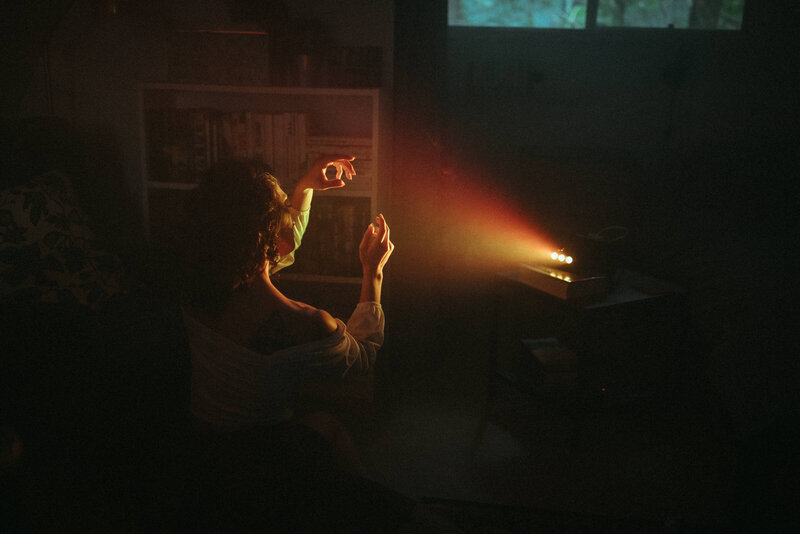 curly hair girl sitting in front of a projector playing with her hands in the warm light