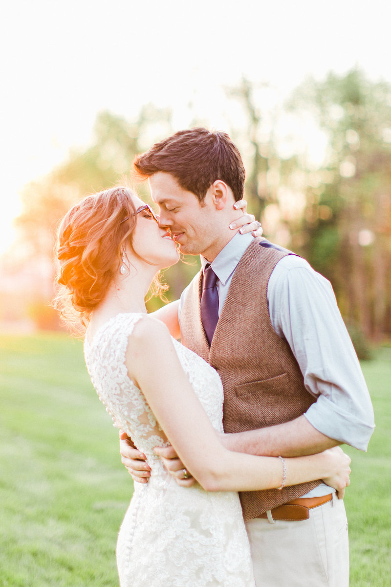 bride and groom embrace and kiss each other at sunset