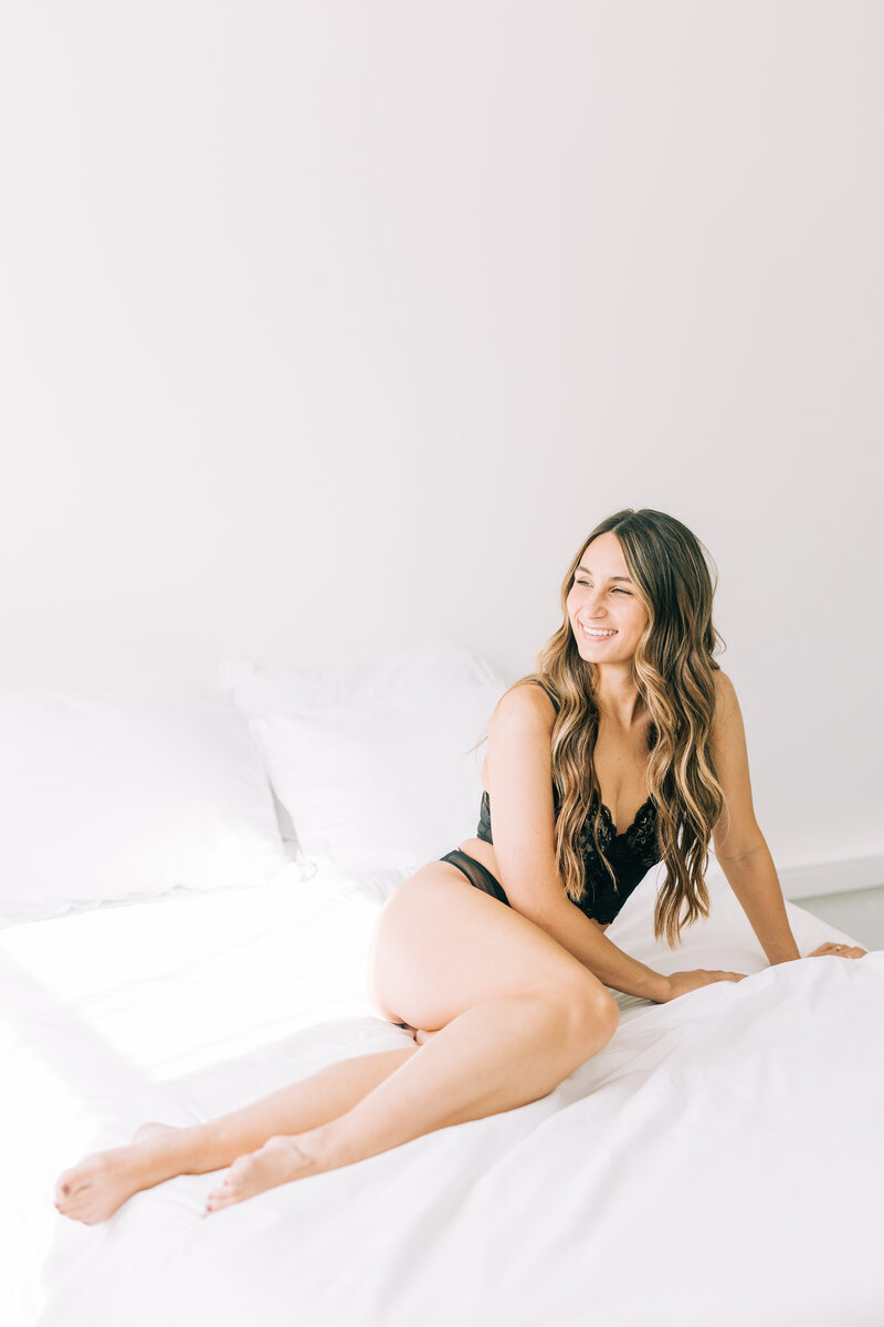 woman smiling on bed wearing black lingerie winx photo knoxville boudoir photographer