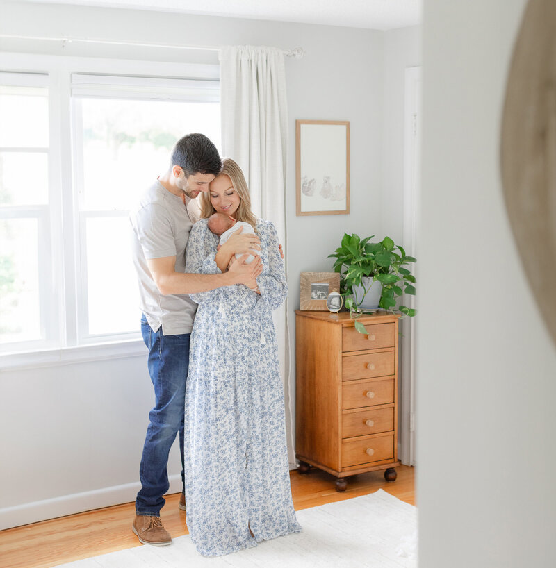 massachusetts mom wearing floral dress holds newborn baby while dad wraps his arms around her