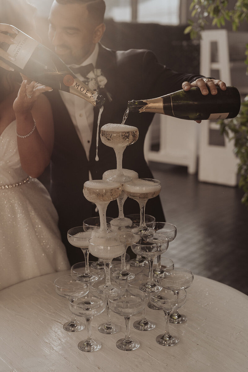 Photo capturing the moment newlyweds pour champagne into a glass tower.