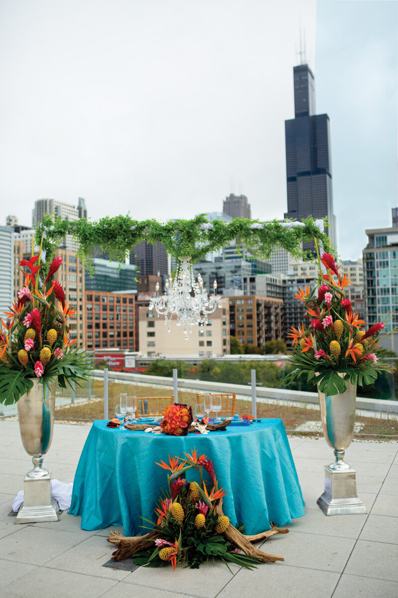 Round table with blue cloth for married couple's reception with colorful floral arch
