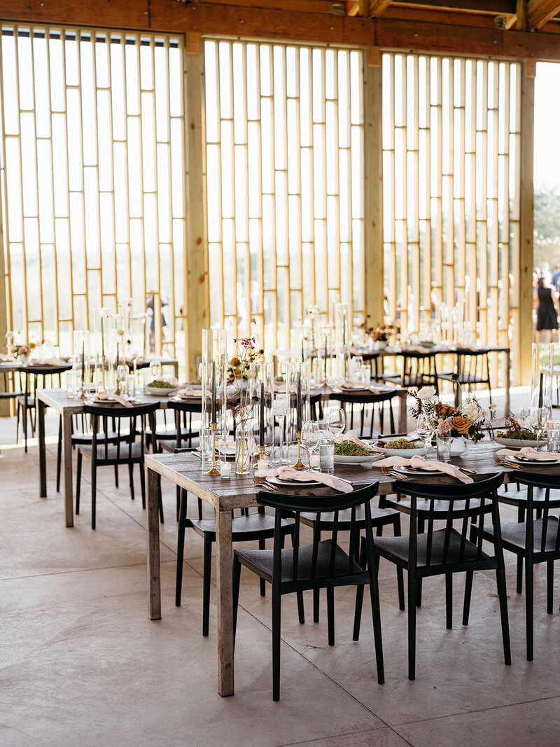 Mid-century modern inspired wedding reception space with bamboo architectural details, simple gray tables, and minimalist black chairs glowing with natural sunlight.