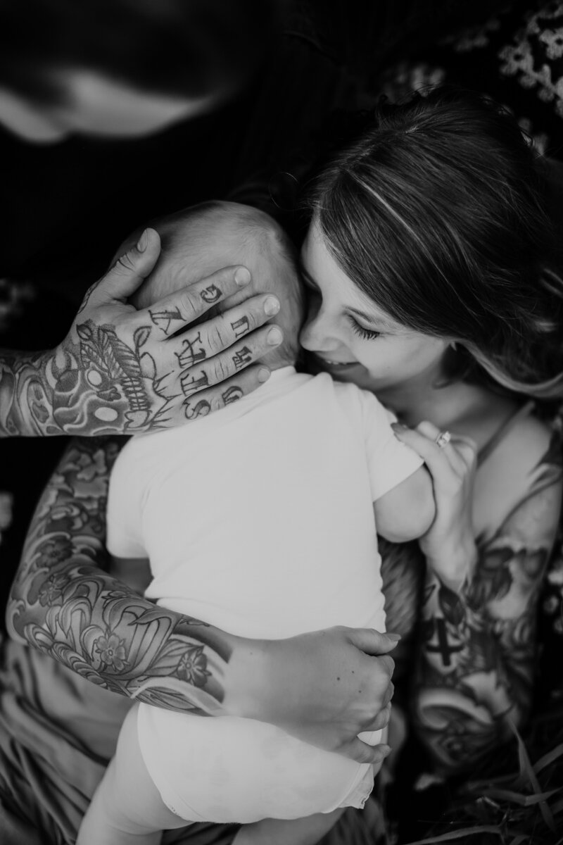 Black and white photo of tattooed hand and mother holding baby