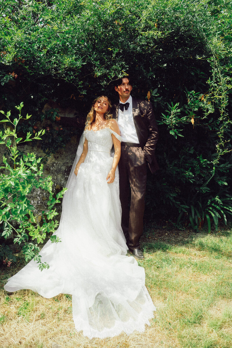 Bride and groom standing together in sunlit Italian greenery, captured in a romantic, cinematic style by a luxury destination wedding photographer UK.