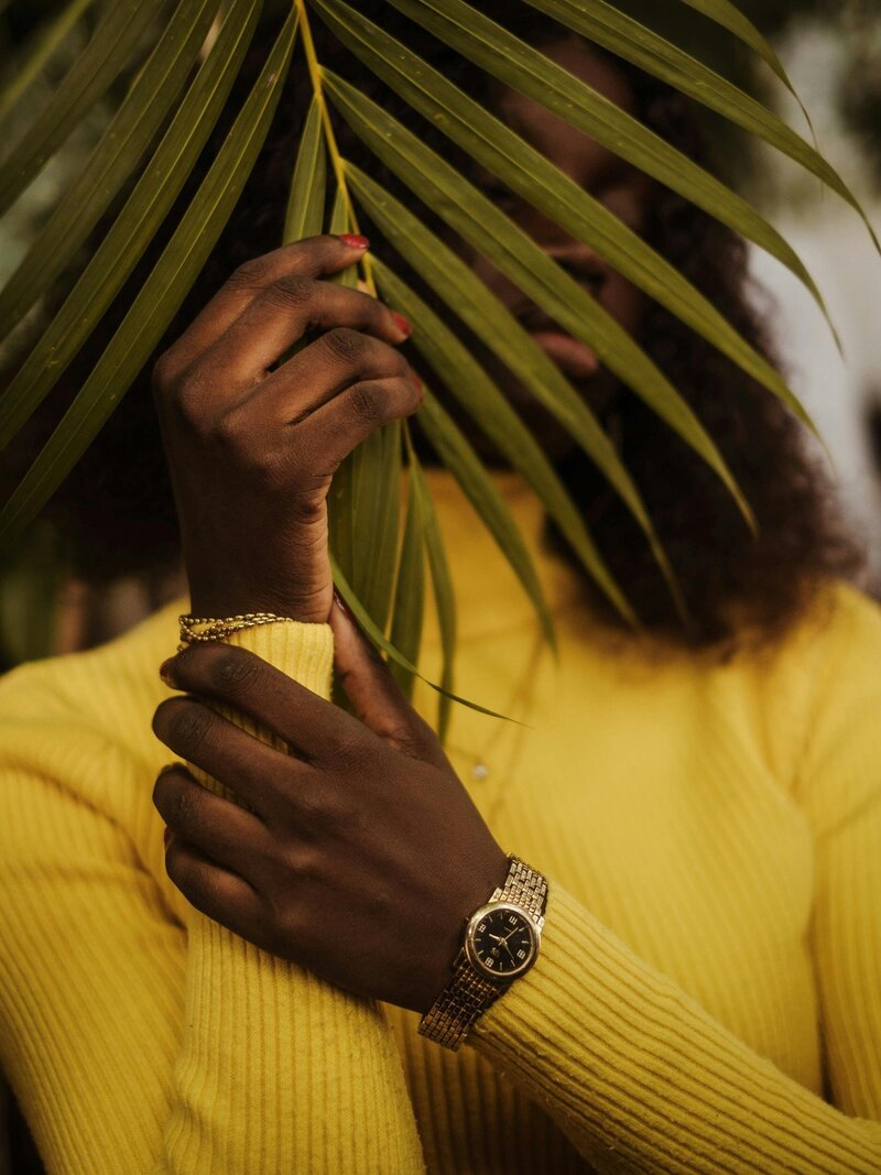Black woman wearing yellow and holding a palm leaf