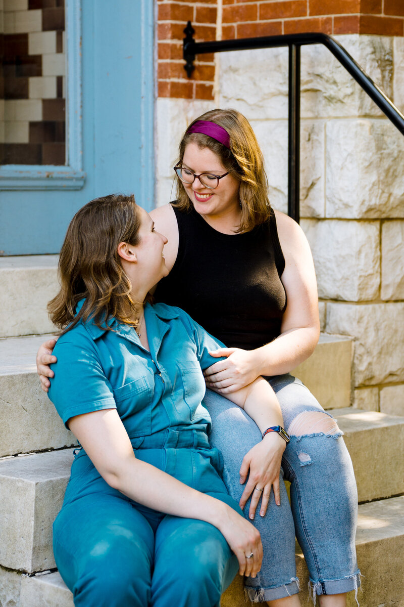 Two women sitting on stairs together while one of them has their arm around the other's shoulder.